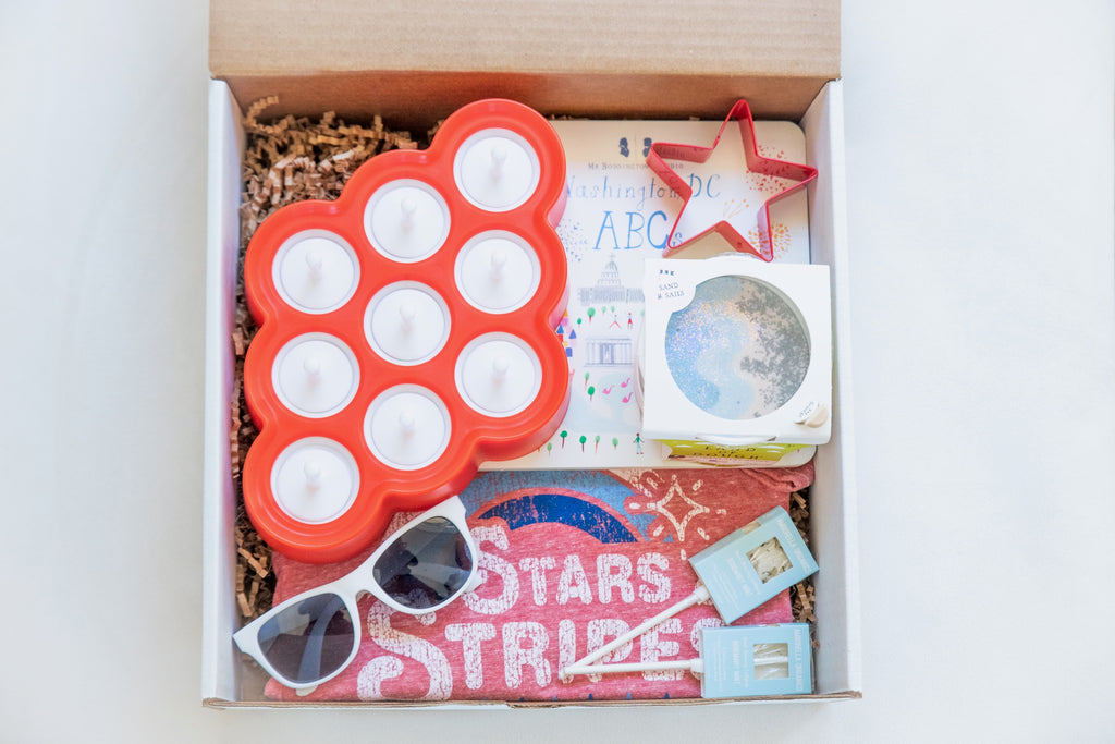 Little Holiday The Tot Box for the 4th of July. Includes Zoku popsicle molds, Washington DC, ABC board book, Land of Dough play dough, red star cookie cutter, custom stars and stripes tshirt design, white toddler sunglasses and two seed-bearing Amborella Organics lollipops in rosemary mint flavor