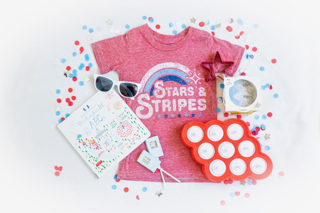 Little Holiday The Tot Box for the 4th of July. Includes Zoku popsicle molds, Washington DC, ABC board book, Land of Dough play dough, red star cookie cutter, custom stars and stripes tshirt design, white toddler sunglasses and two seed-bearing Amborella Organics lollipops in rosemary mint flavor. Fourth of July confetti.